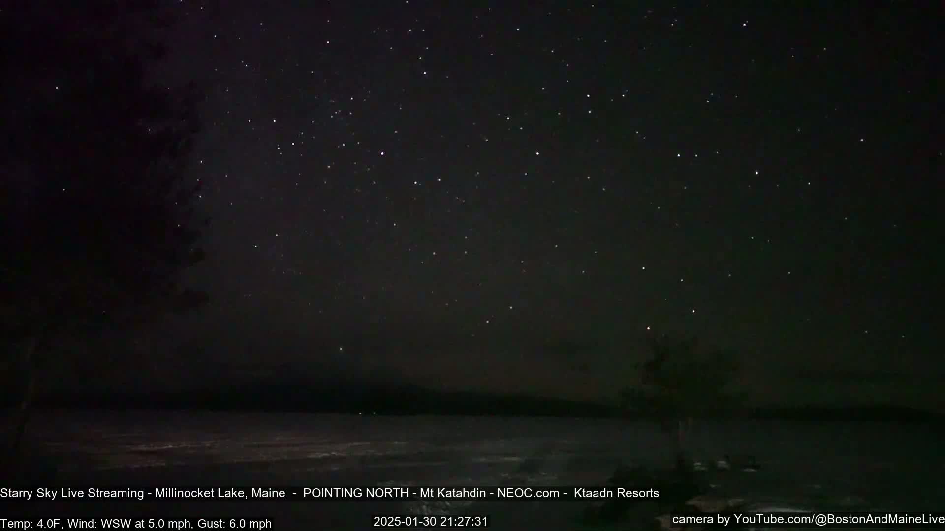A nighttime view of a calm lake under a clear, starry sky with a gentle wind.