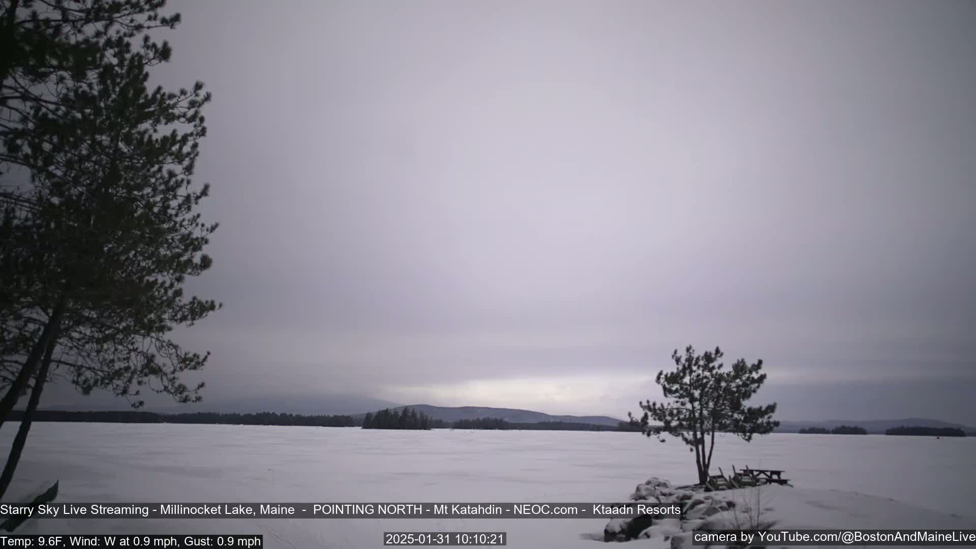 A snow-covered lake stretches to a distant, faintly lit mountain range under an overcast sky.