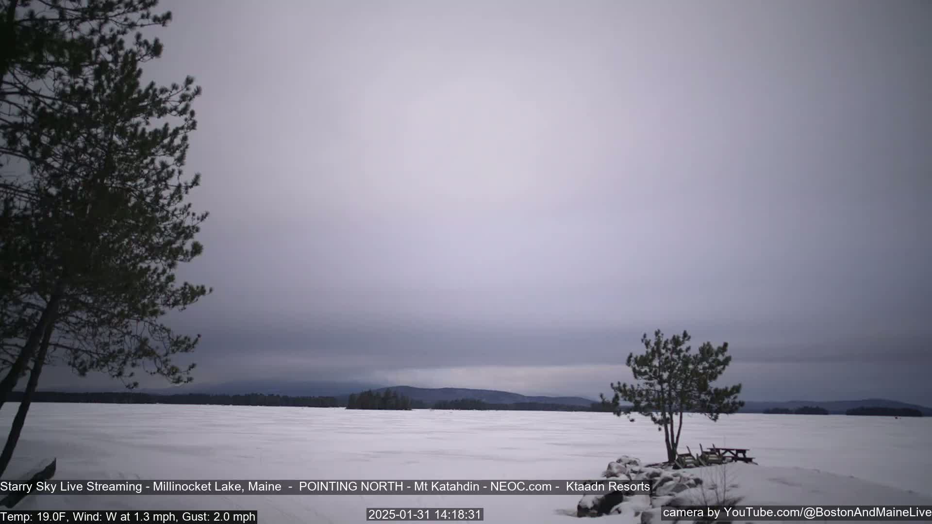 A snow-covered lake stretches to distant, low hills under a cloudy, overcast sky.