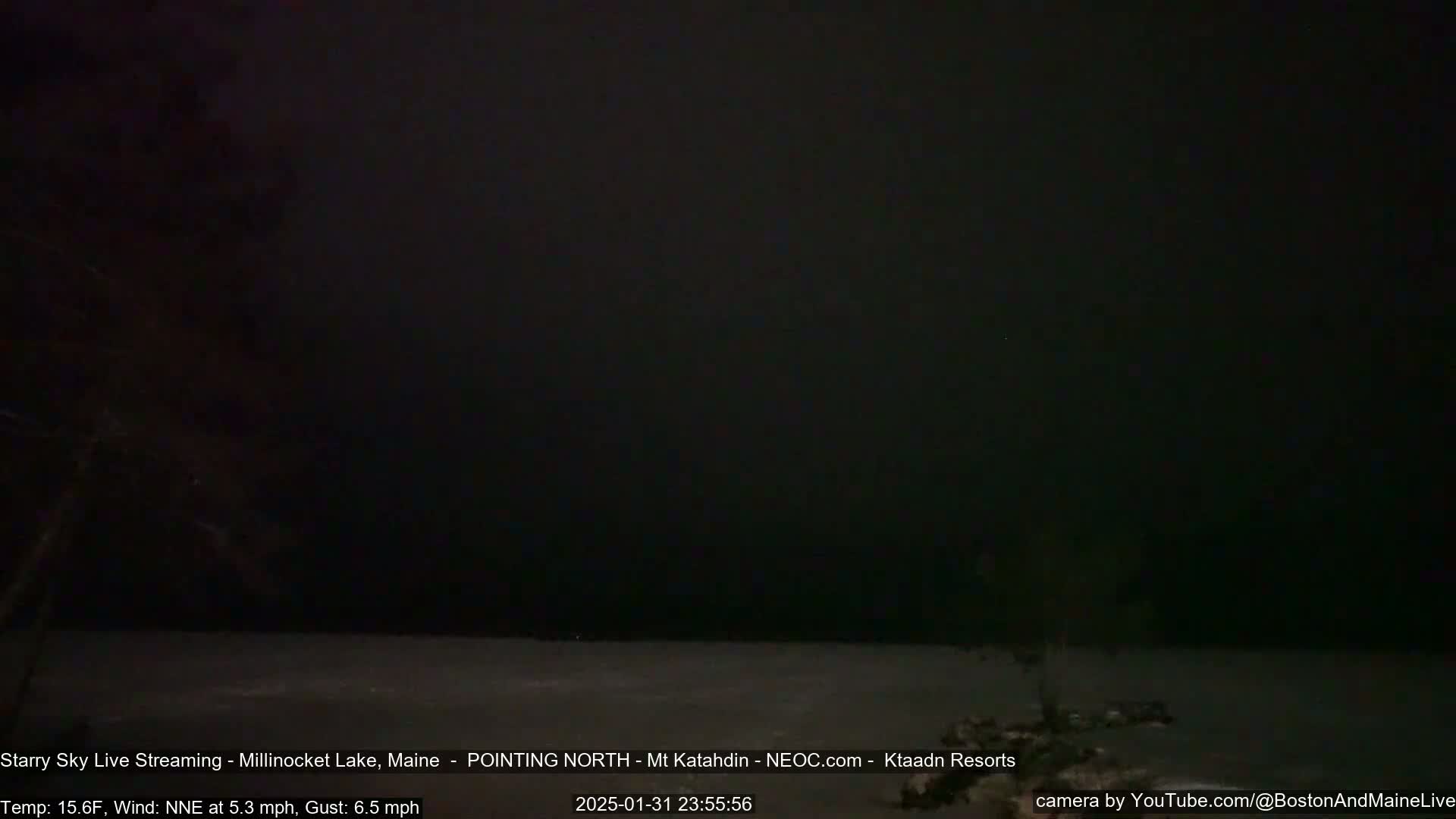A dark, starry night sky over a still body of water under a NNE wind.