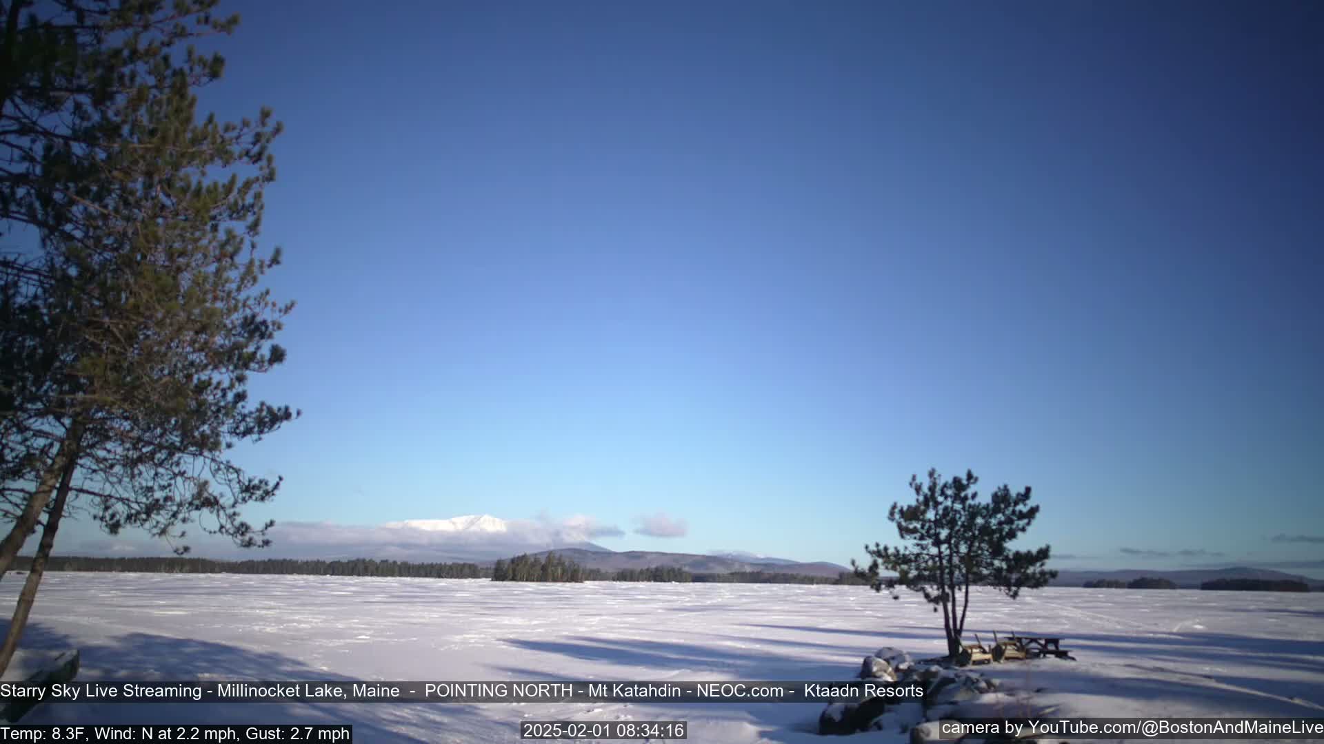 A snow-covered lake stretches to a distant mountain range under a clear, bright blue sky.