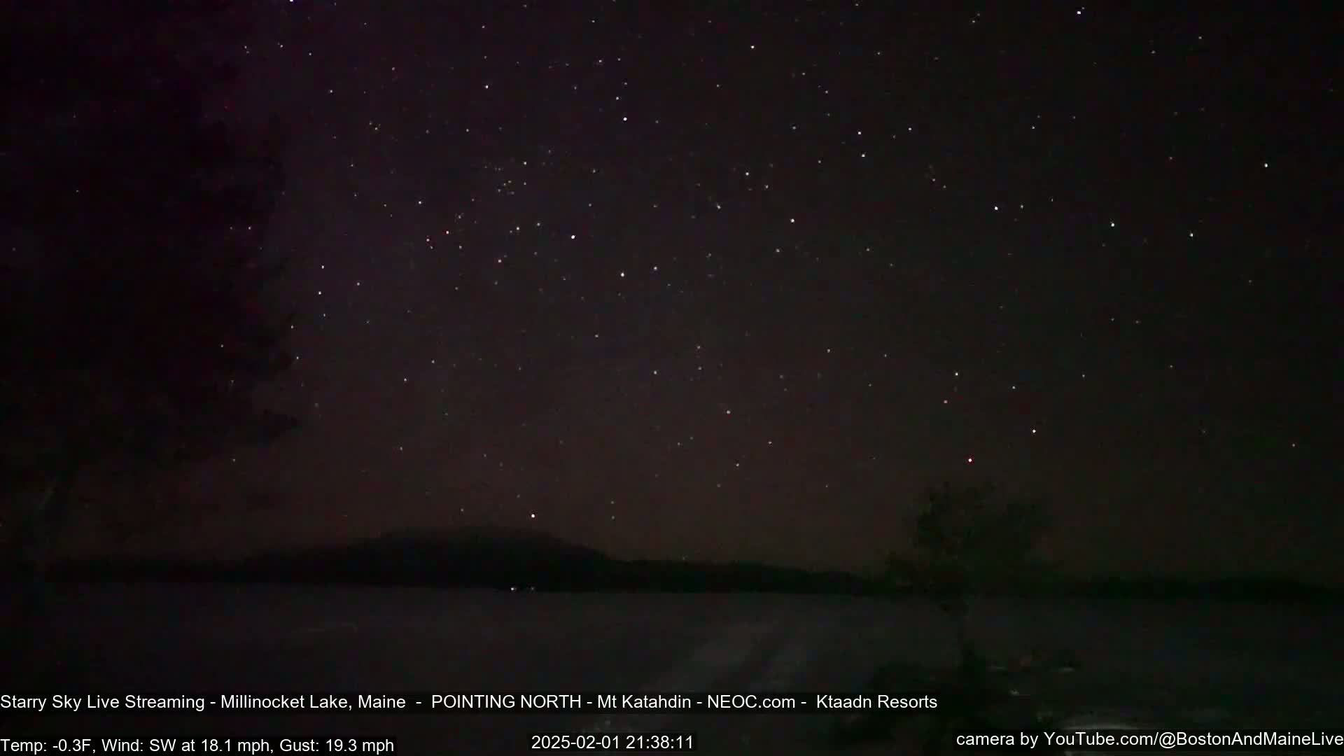 A dark, starry night sky over a calm lake with a distant mountain range, under a cold wind.