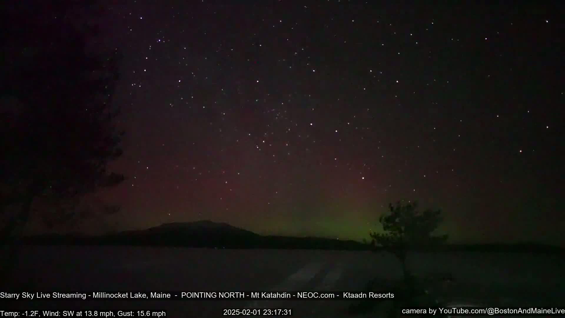 A nighttime view of a lake and distant mountains under a starry sky displaying a faint aurora borealis, with a southwest wind at 13.8 mph and gusts up to 15.6 mph, and a temperature of -1.2°F.