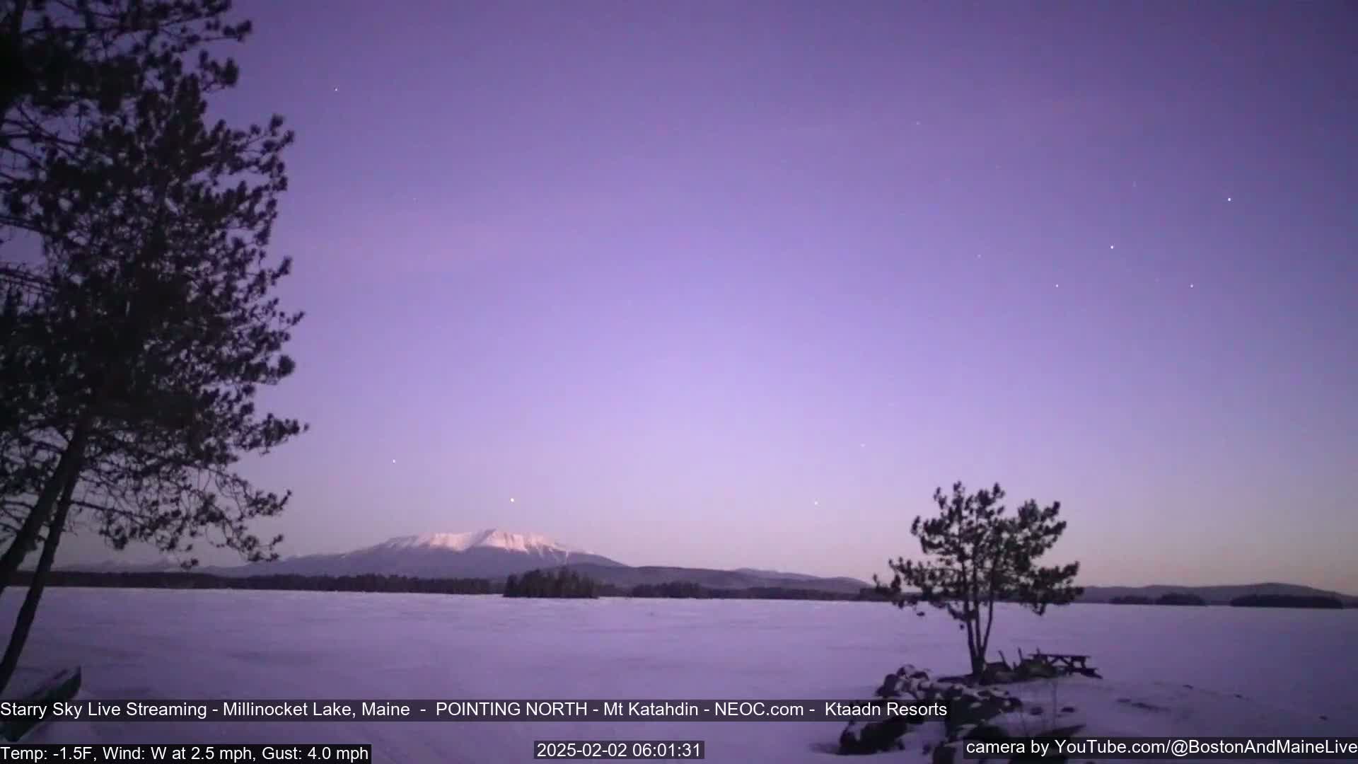A snow-covered lake stretches to a distant, snow-capped mountain under a twilight sky with a few visible stars.