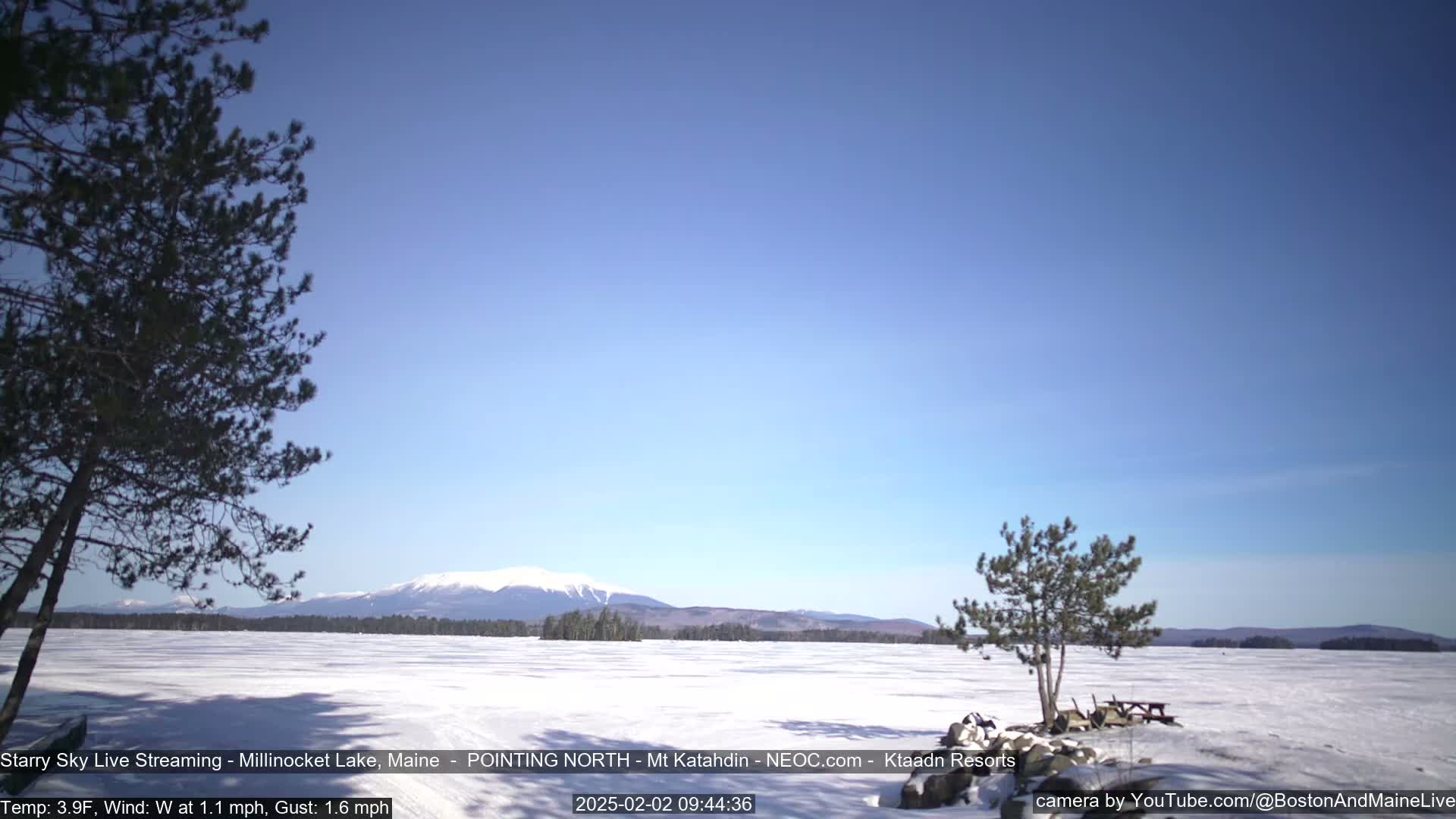 A snow-covered lake stretches to a distant mountain range under a clear blue sky.