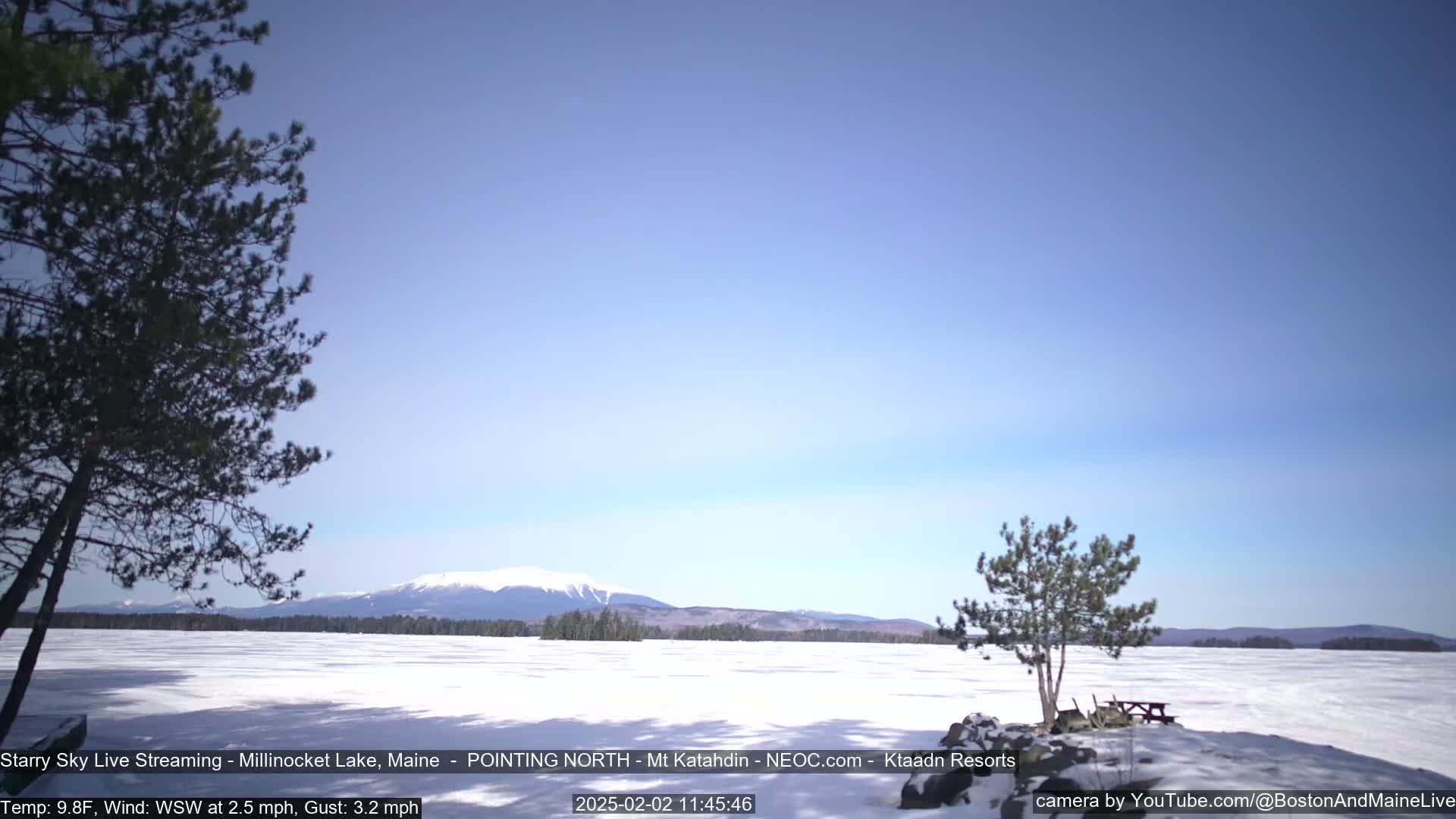 A snow-covered lake stretches to a distant mountain range under a clear, light-blue sky.