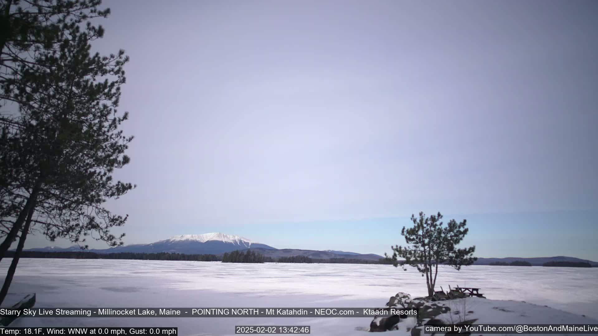 A snow-covered lake stretches to a distant mountain range under a pale, clear sky.