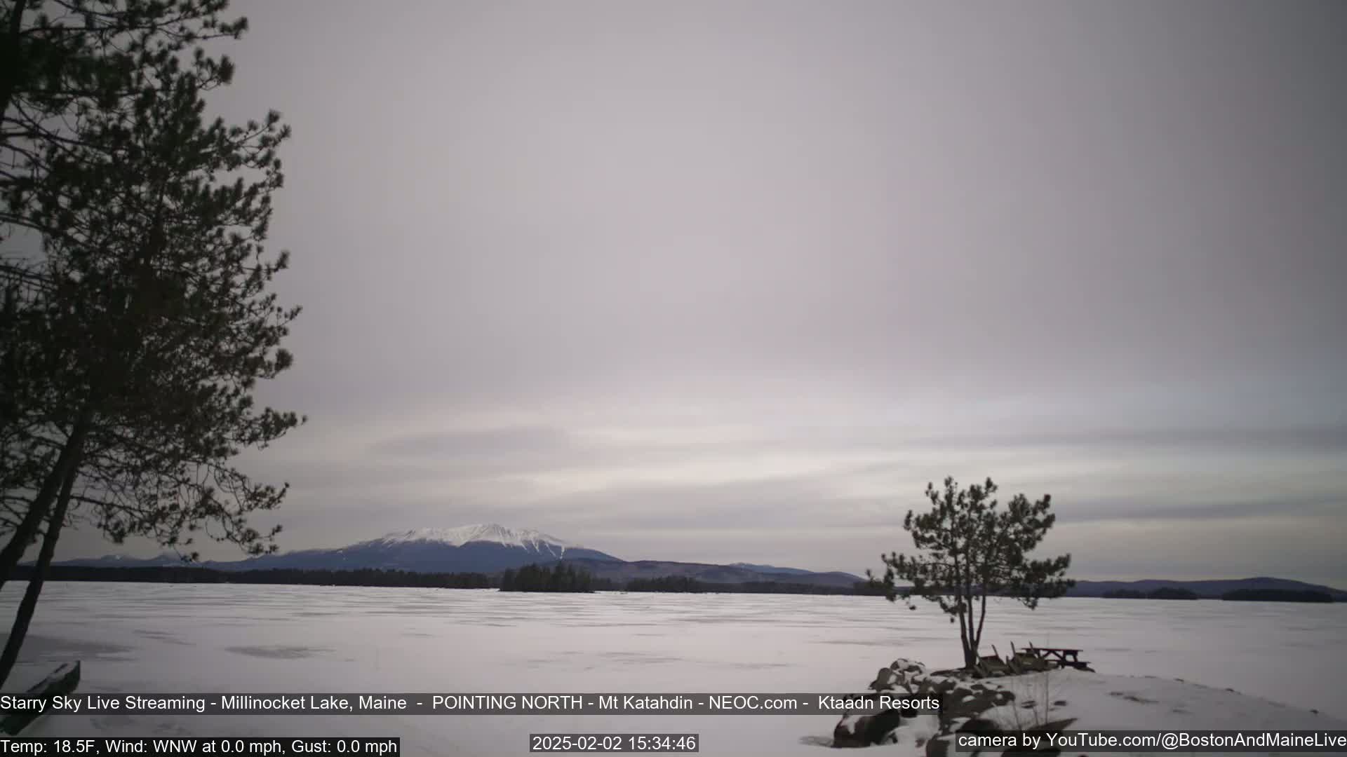 A snow-covered lake stretches to a distant, snow-capped mountain range under a pale gray sky.