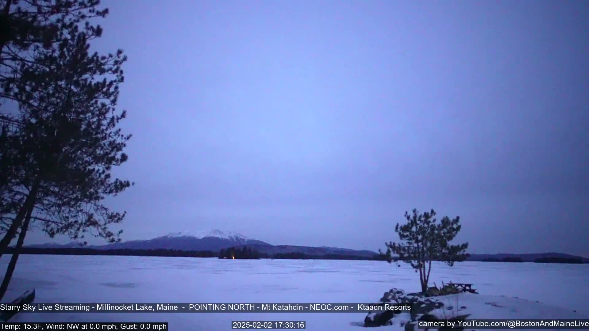 A snow-covered lake stretches to a distant mountain range under a twilight sky.