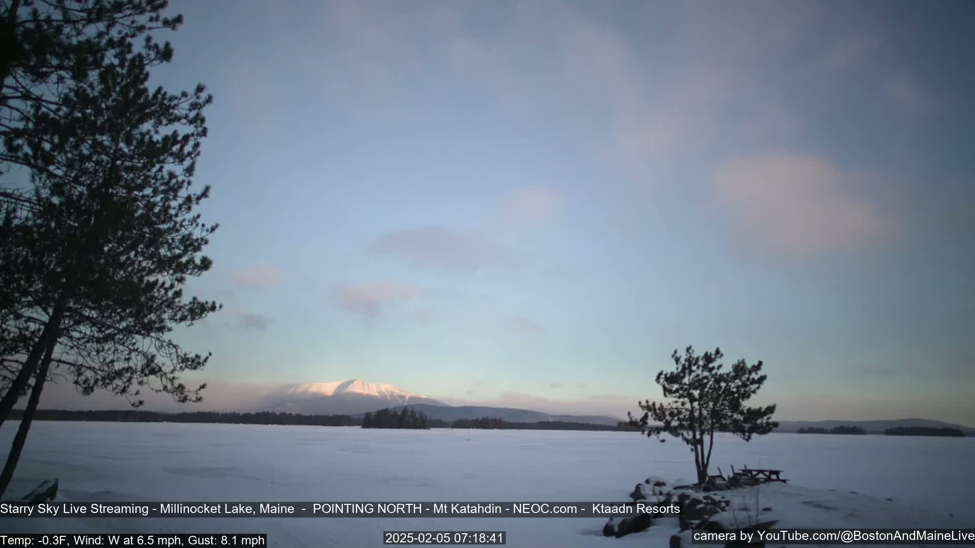 A snow-covered lake stretches to a distant, snow-capped mountain under a pale, partly cloudy sky.