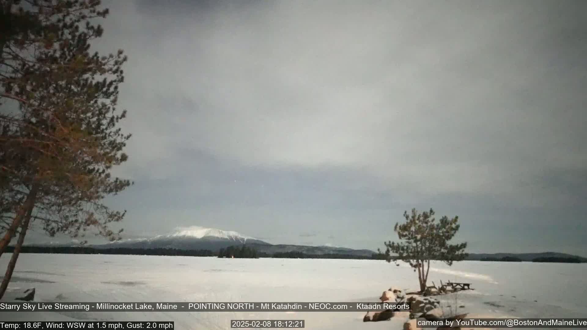 A snow-covered lake stretches to a distant, snow-capped mountain under a cloudy, twilight sky.