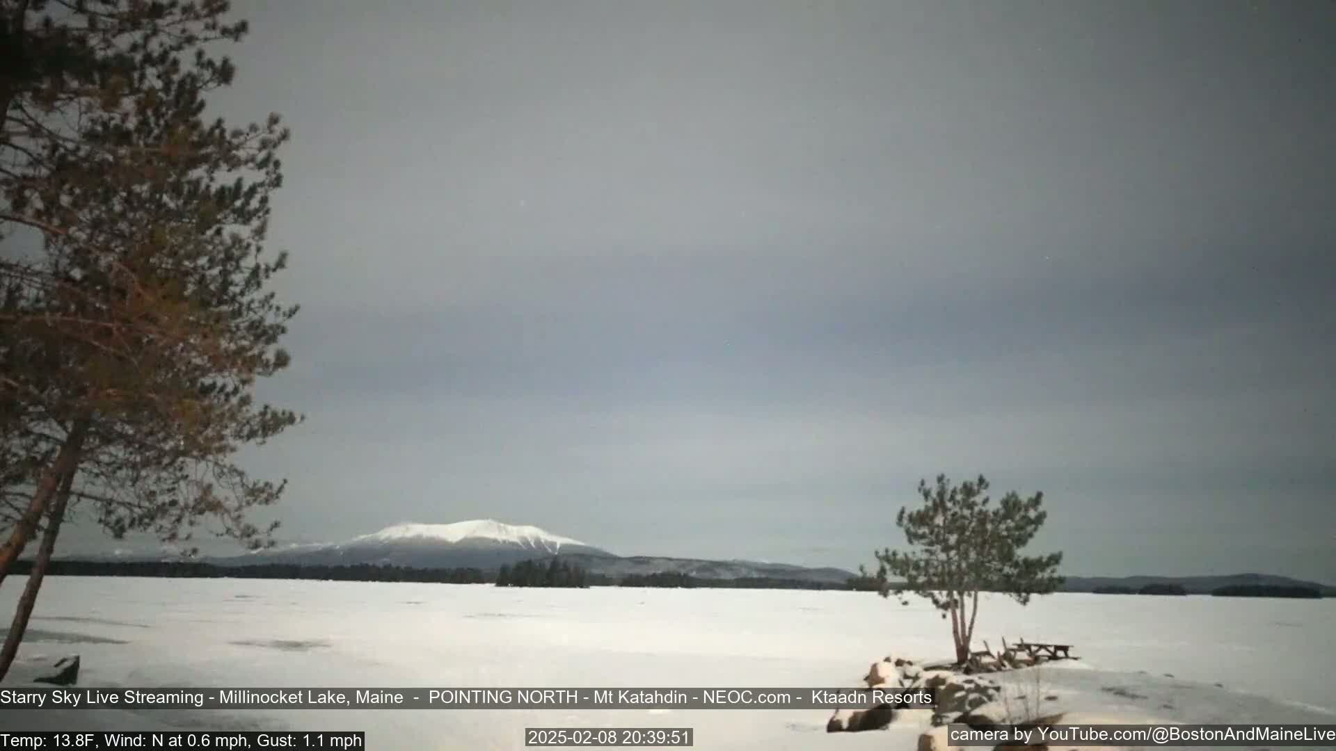 A snow-covered lake stretches to a distant mountain range under a cloudy, gray sky.