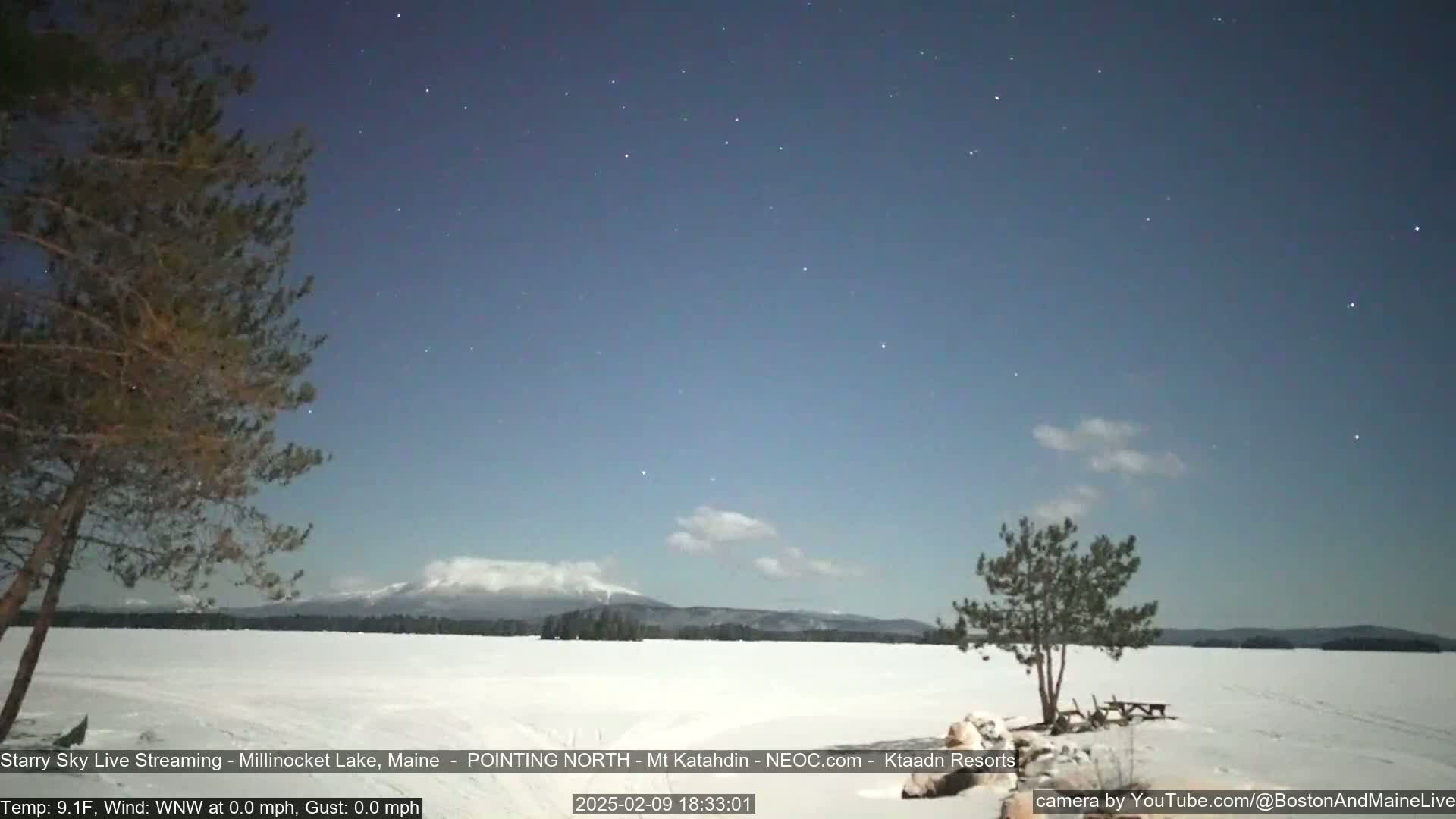 A snow-covered frozen lake stretches to a mountainous horizon under a clear, starry night sky.