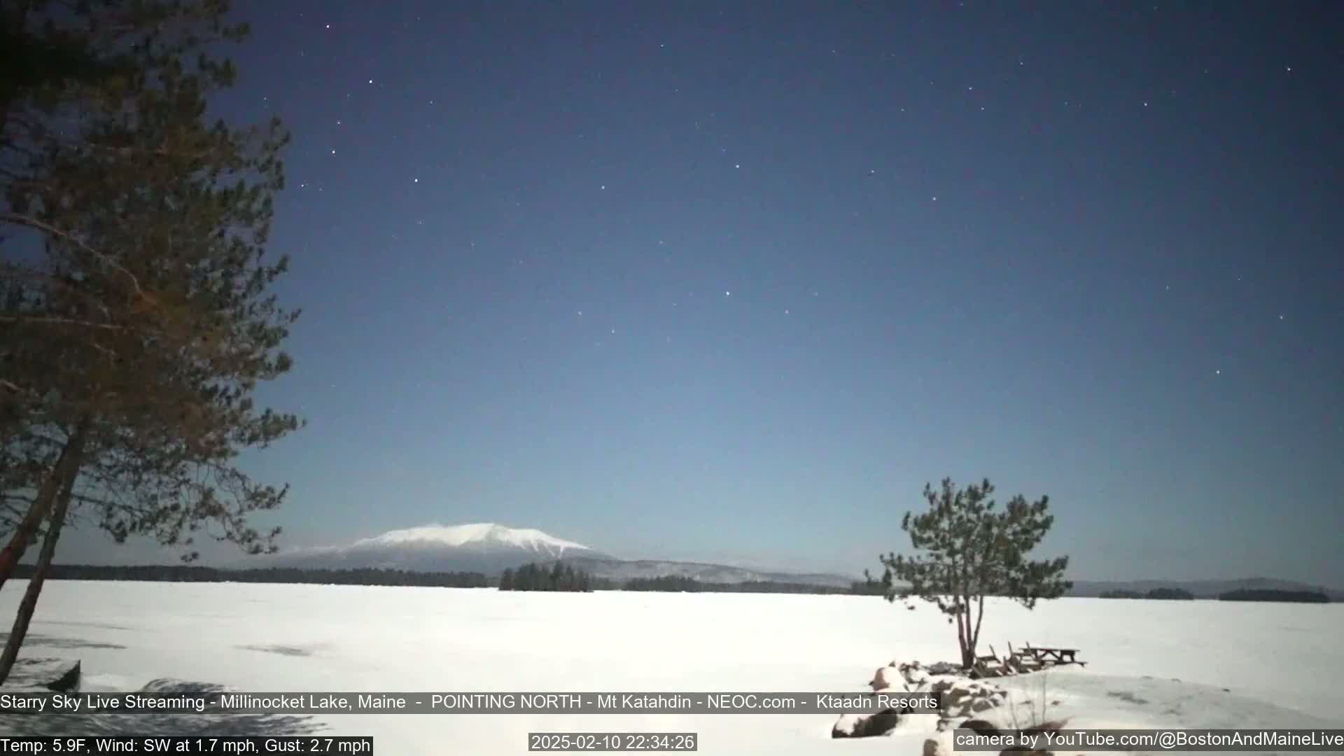A snow-covered frozen lake stretches to a distant, snow-capped mountain under a clear, starry night sky.