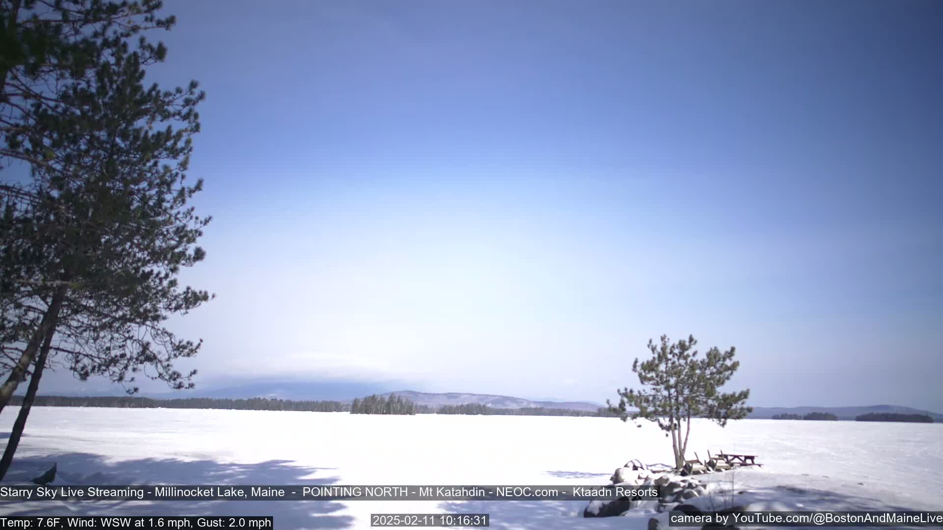 A snow-covered lake stretches to a distant mountain range under a clear blue sky.