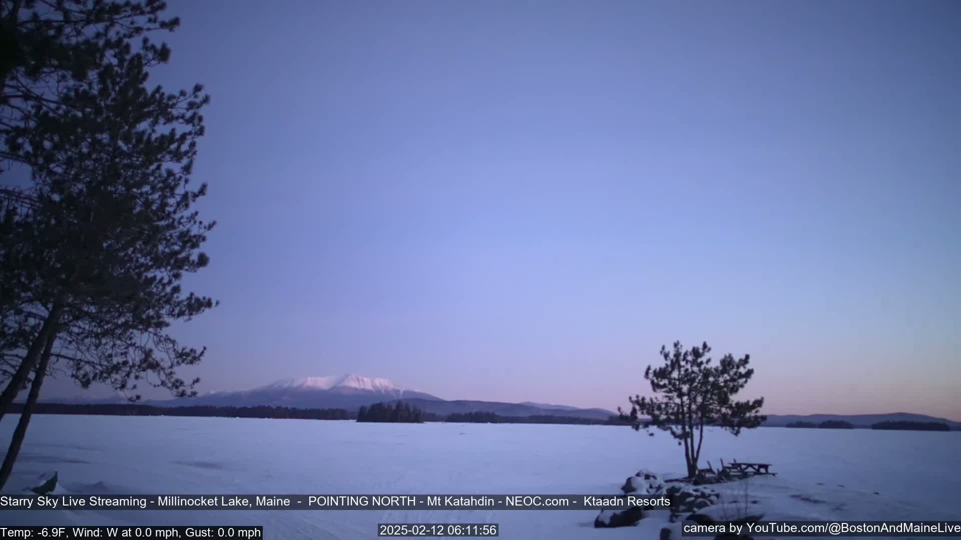 A snow-covered lake and distant mountain range are visible under a twilight sky.
