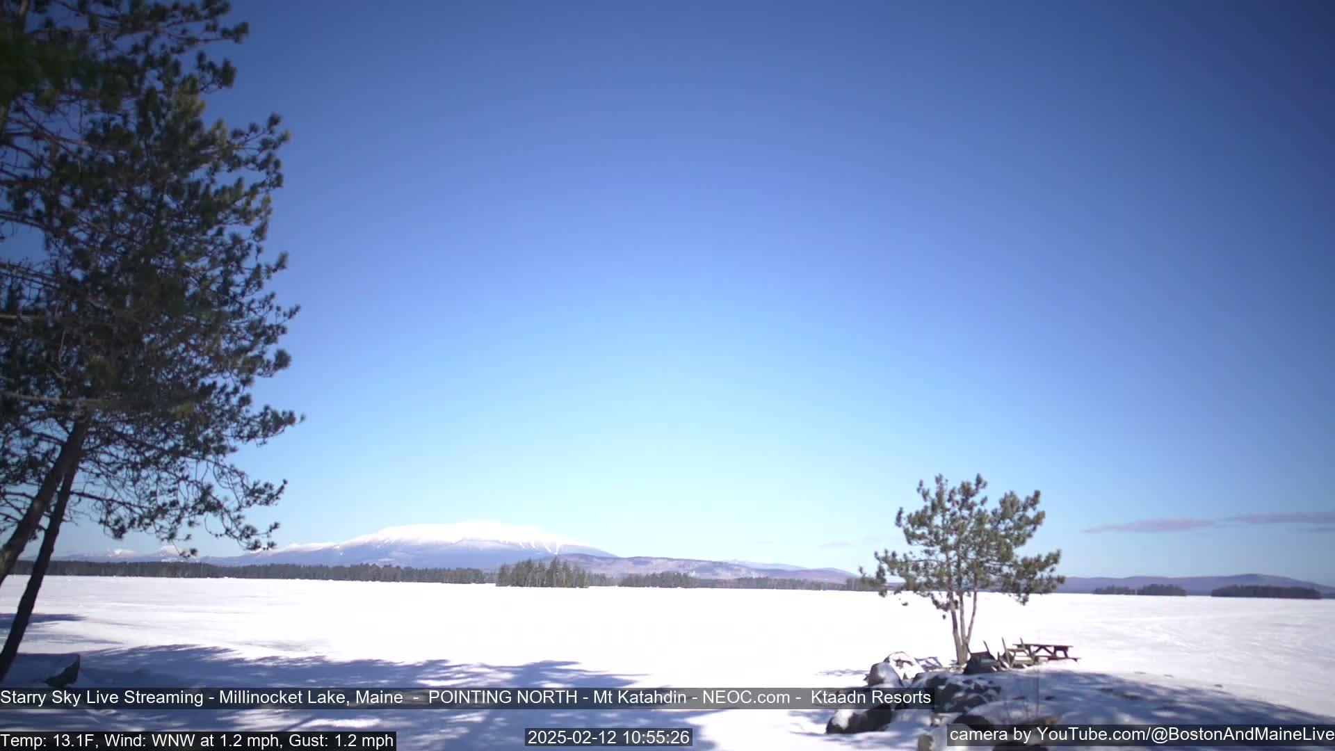 A snow-covered lake stretches to a distant mountain range under a clear blue sky.