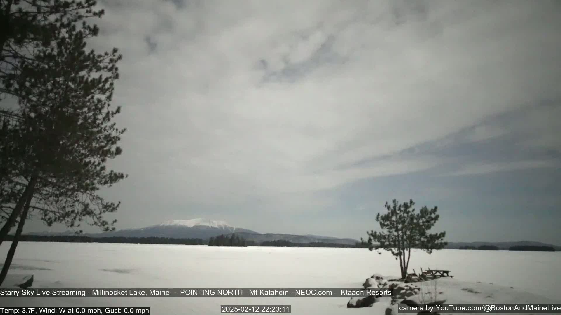 A snow-covered lake stretches to a distant, snow-capped mountain range under a cloudy sky.