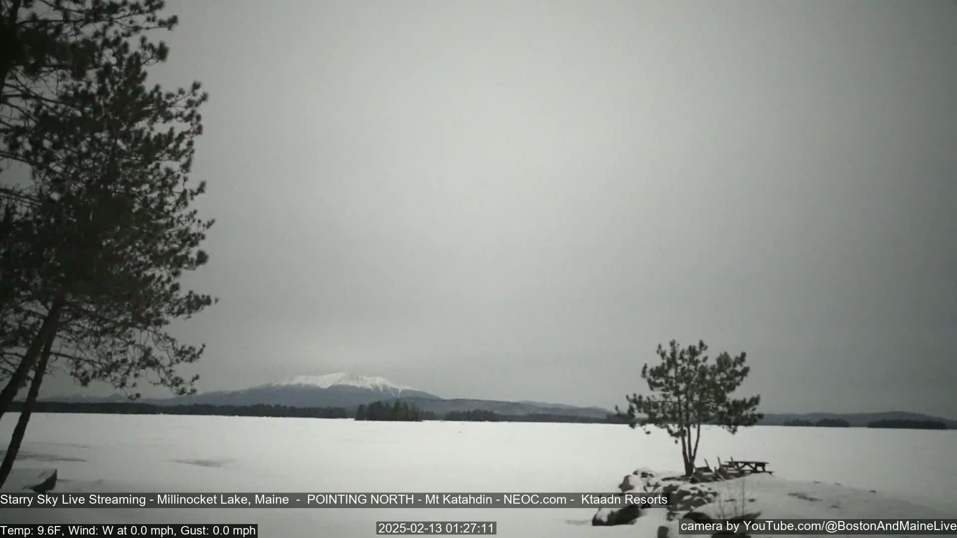 A snow-covered lake stretches to a distant, snow-capped mountain range under a gray, overcast sky.