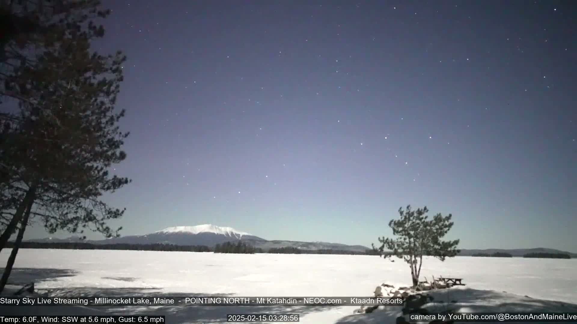A snow-covered lake stretches out before a distant, snow-capped mountain under a starry, twilight sky.