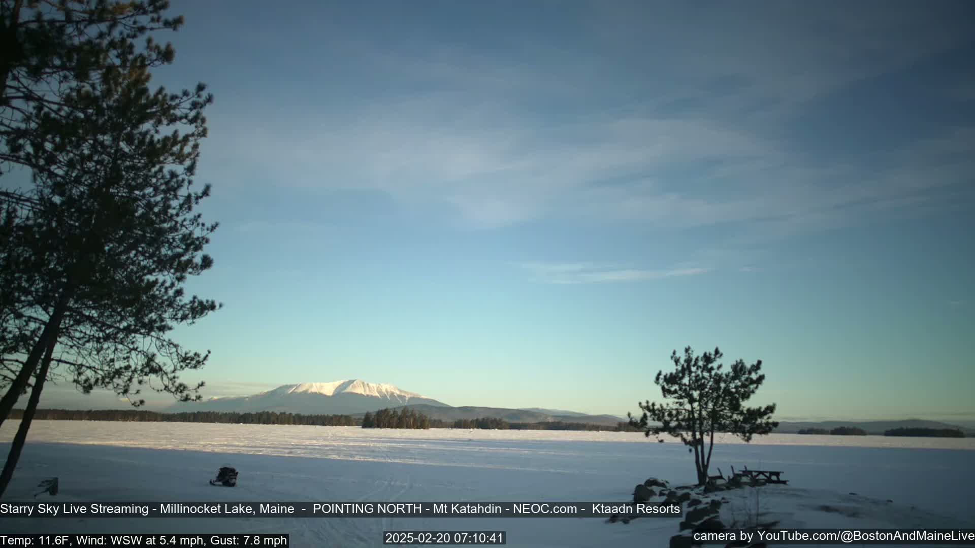 A snow-covered lake stretches to a distant mountain range under a clear, light-blue sky.