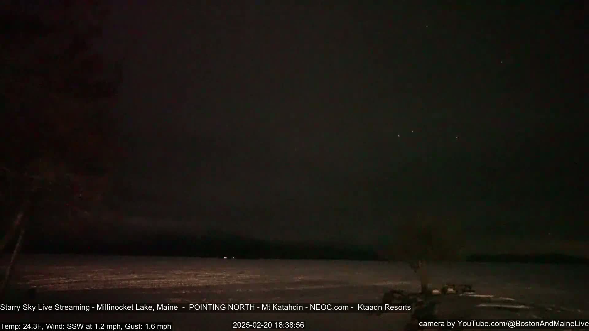 A nighttime long shot of a dark, still lake under a clear, starry sky with a slight wind.