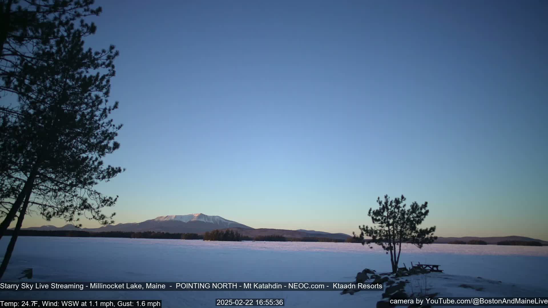 A snow-covered lake stretches to a mountain range under a clear, twilight sky.