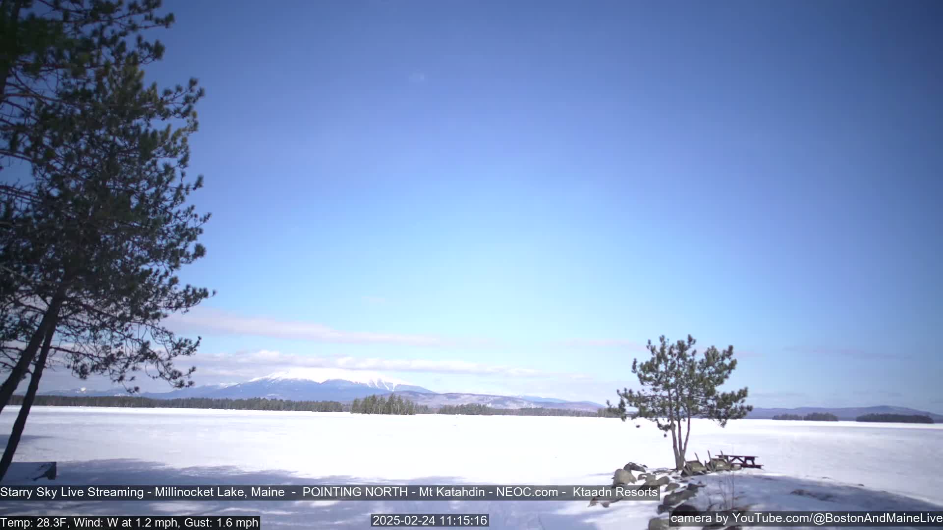 A snow-covered lake stretches to a distant mountain range under a clear blue sky.