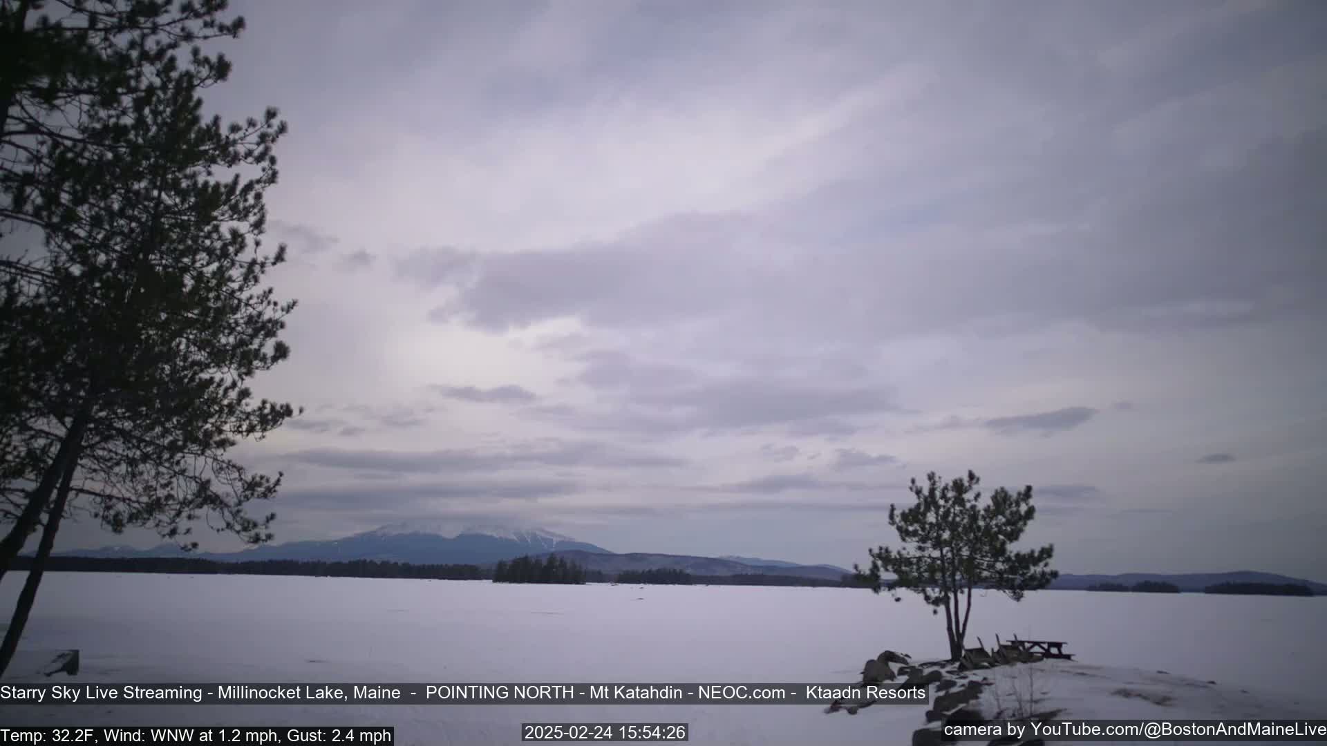 A snow-covered lake stretches to a distant mountain range under a cloudy sky.