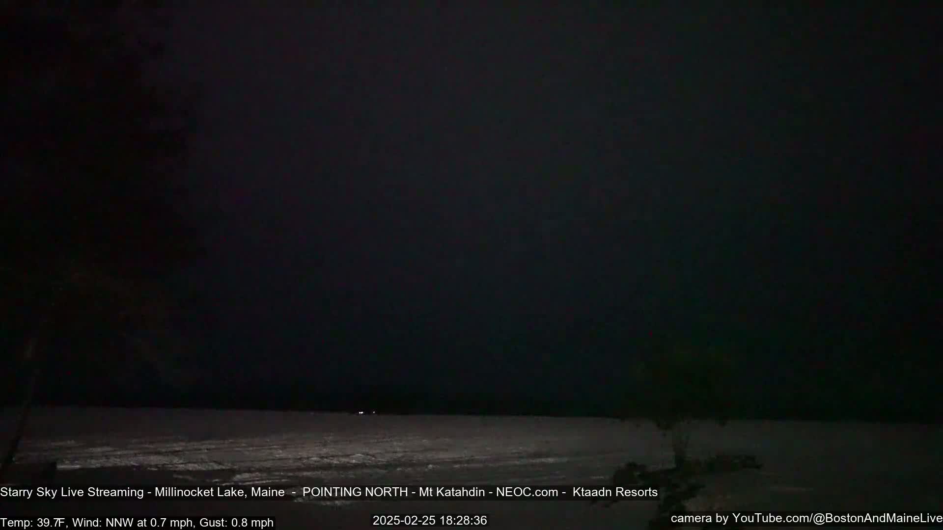 A dark, starry night scene shows a mostly frozen lake under a nearly cloudless sky, with a gentle north-northwest wind.
