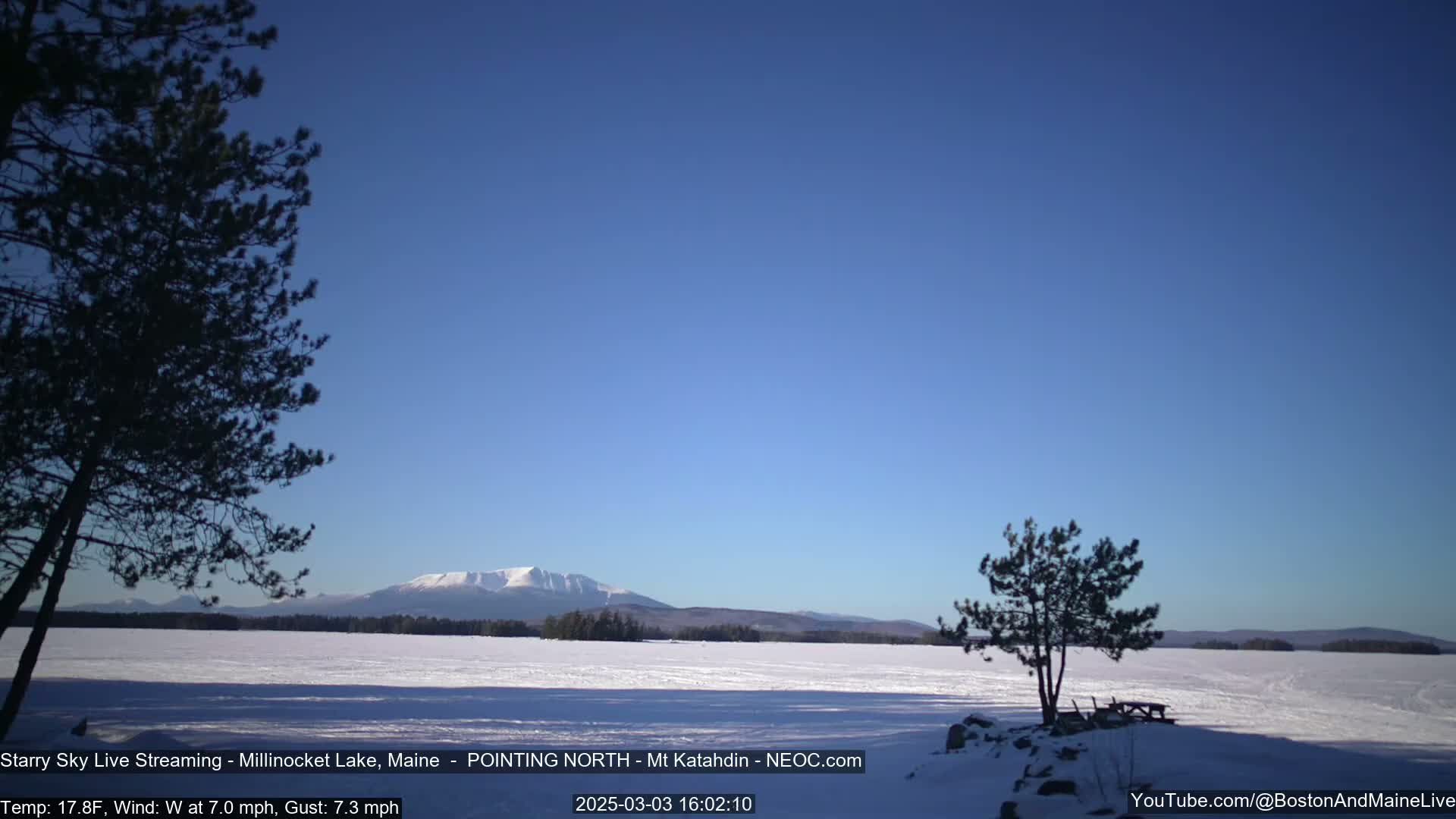 A snow-covered lake stretches to a distant mountain range under a clear blue sky.