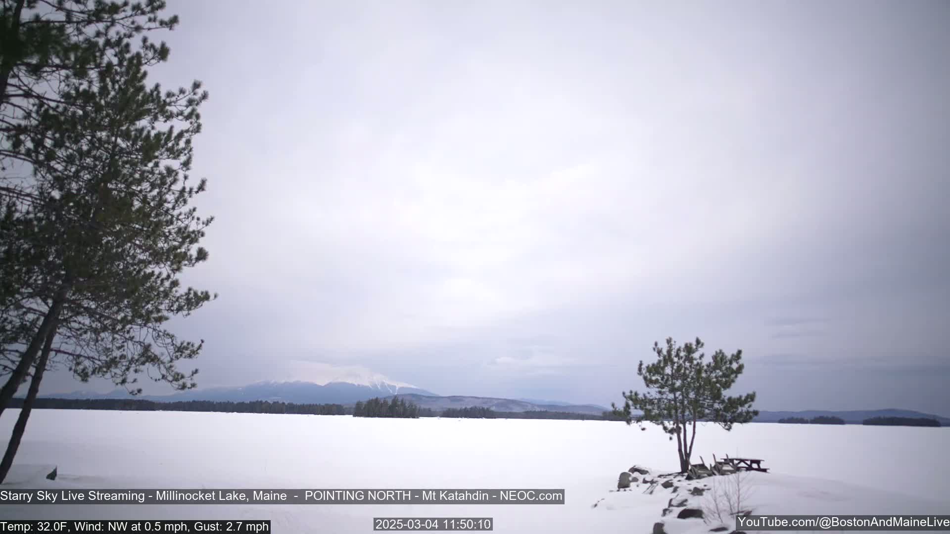 A snow-covered lake stretches to a distant mountain range under a lightly cloudy sky.