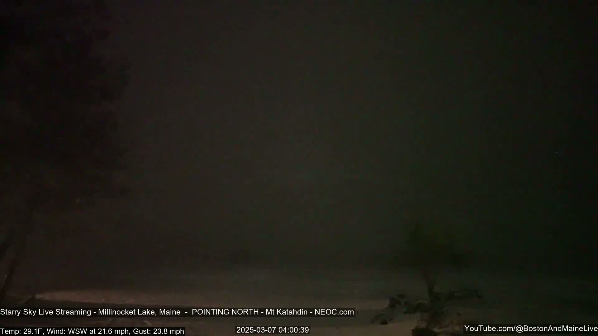 A dark, nighttime scene shows a snow-covered ground under a heavy, dark sky with a strong west-southwest wind.