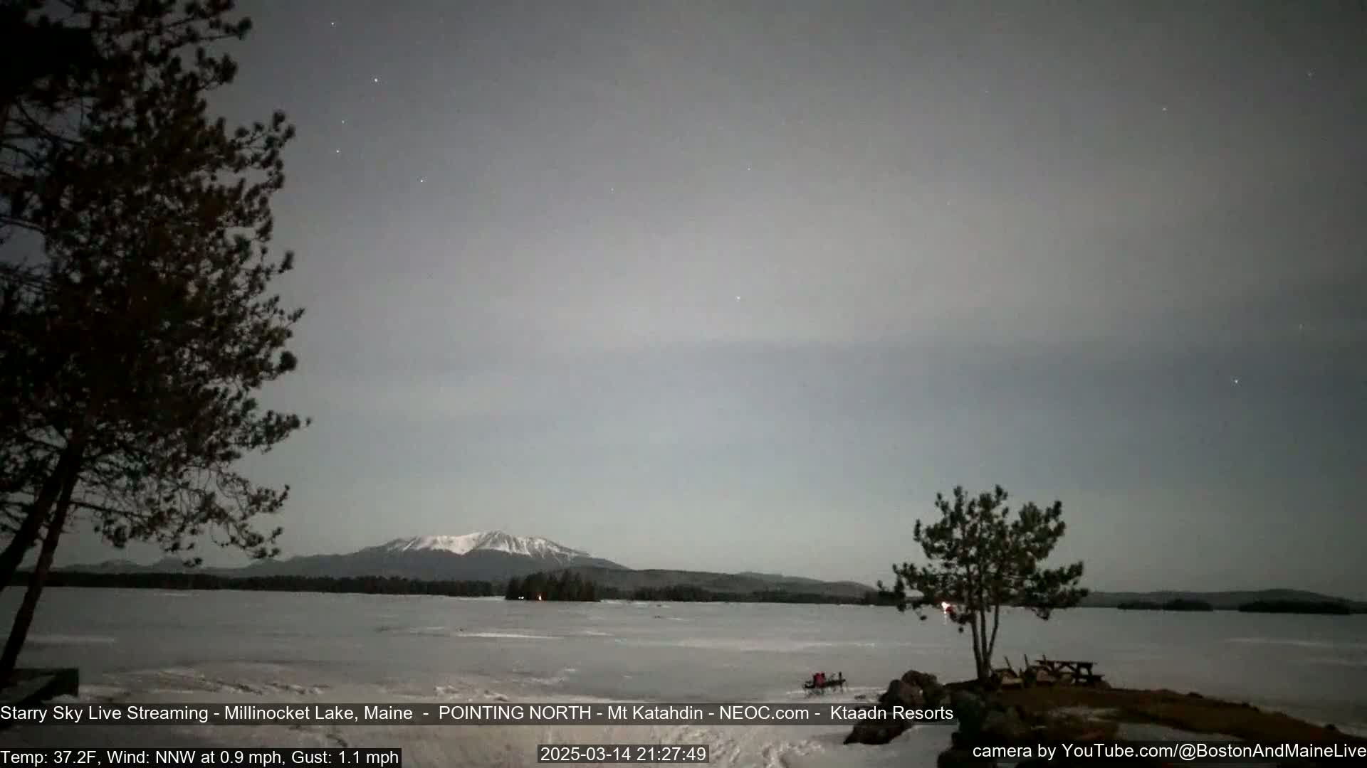 A snow-capped mountain is visible across a mostly frozen lake under a twilight sky dotted with stars.