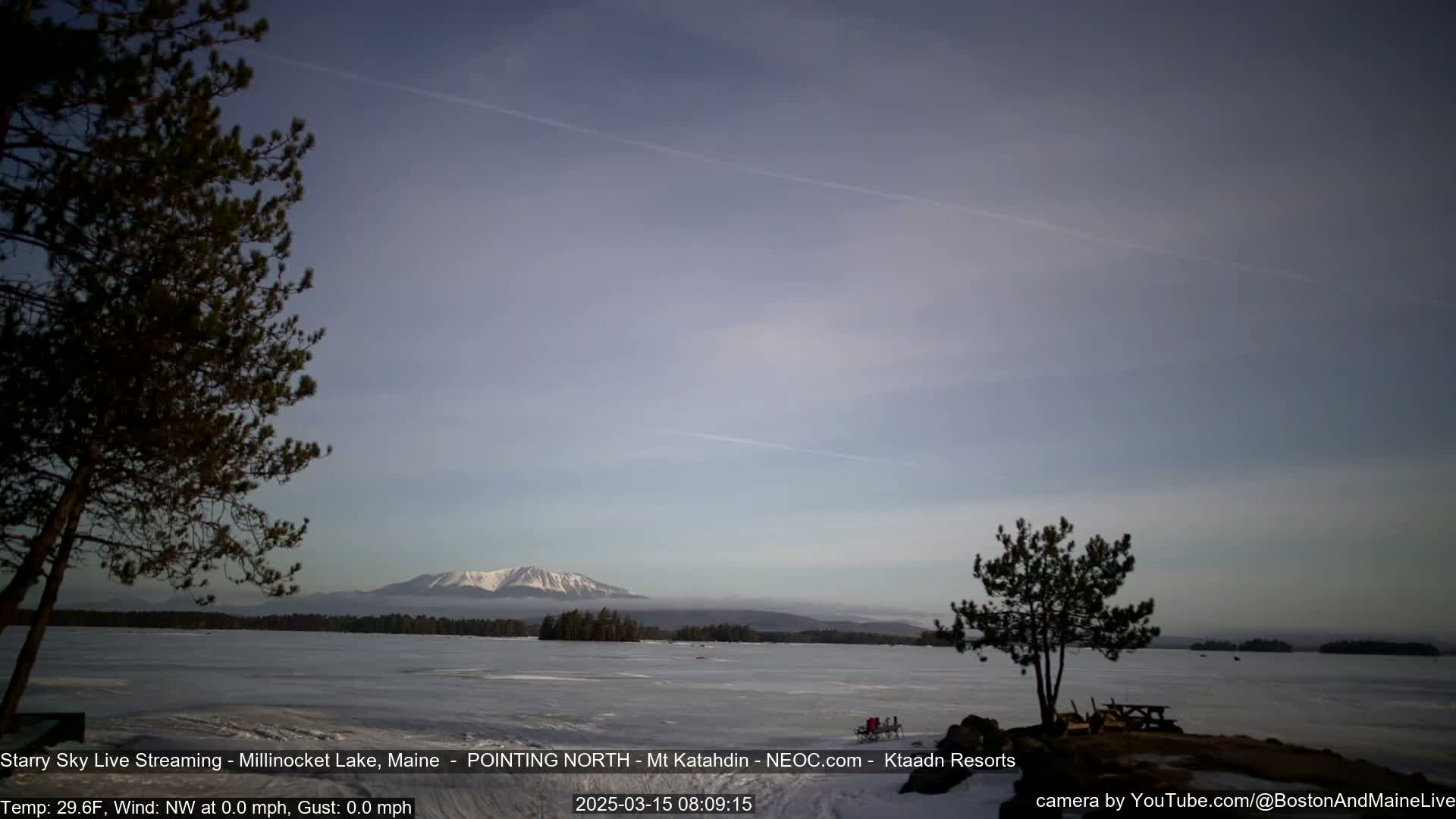 A snow-capped mountain is visible in the distance across a partially frozen lake under a mostly clear, light blue sky.