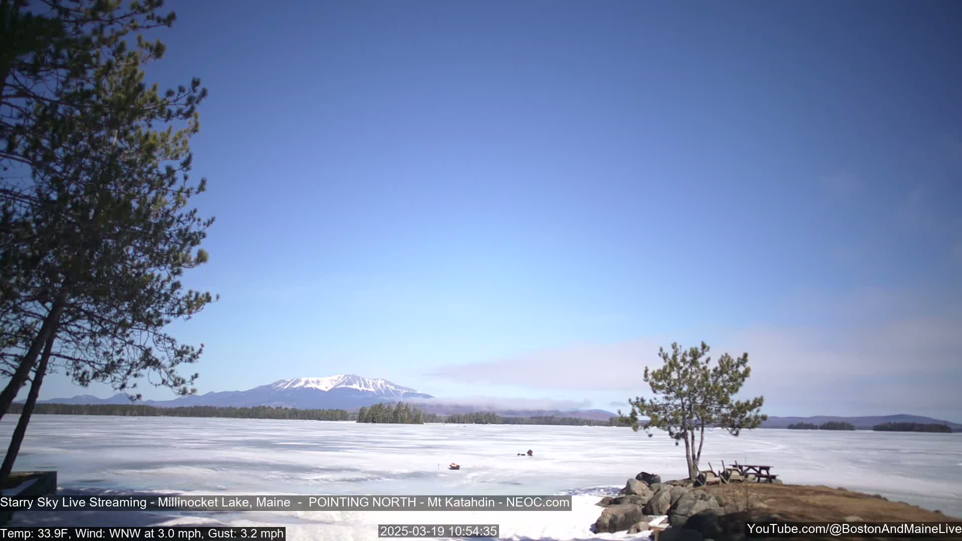 A frozen lake stretches to snow-capped mountains under a clear blue sky.