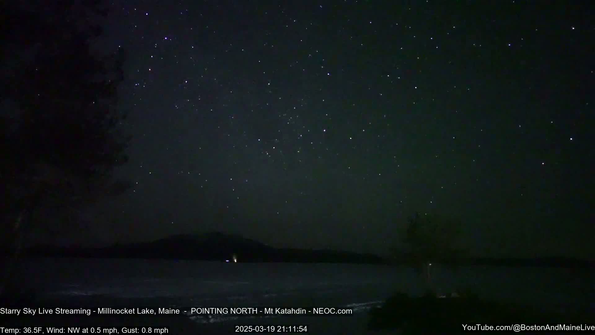 A nighttime view of a star-filled sky over a dark lake under a clear sky with a light northwest wind.