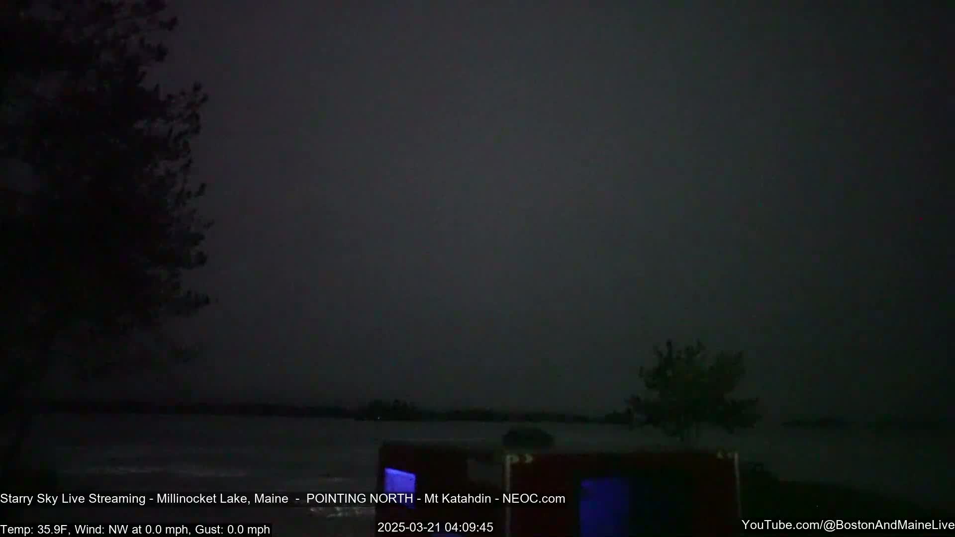 A dark, nighttime scene shows a calm body of water under a mostly overcast sky.