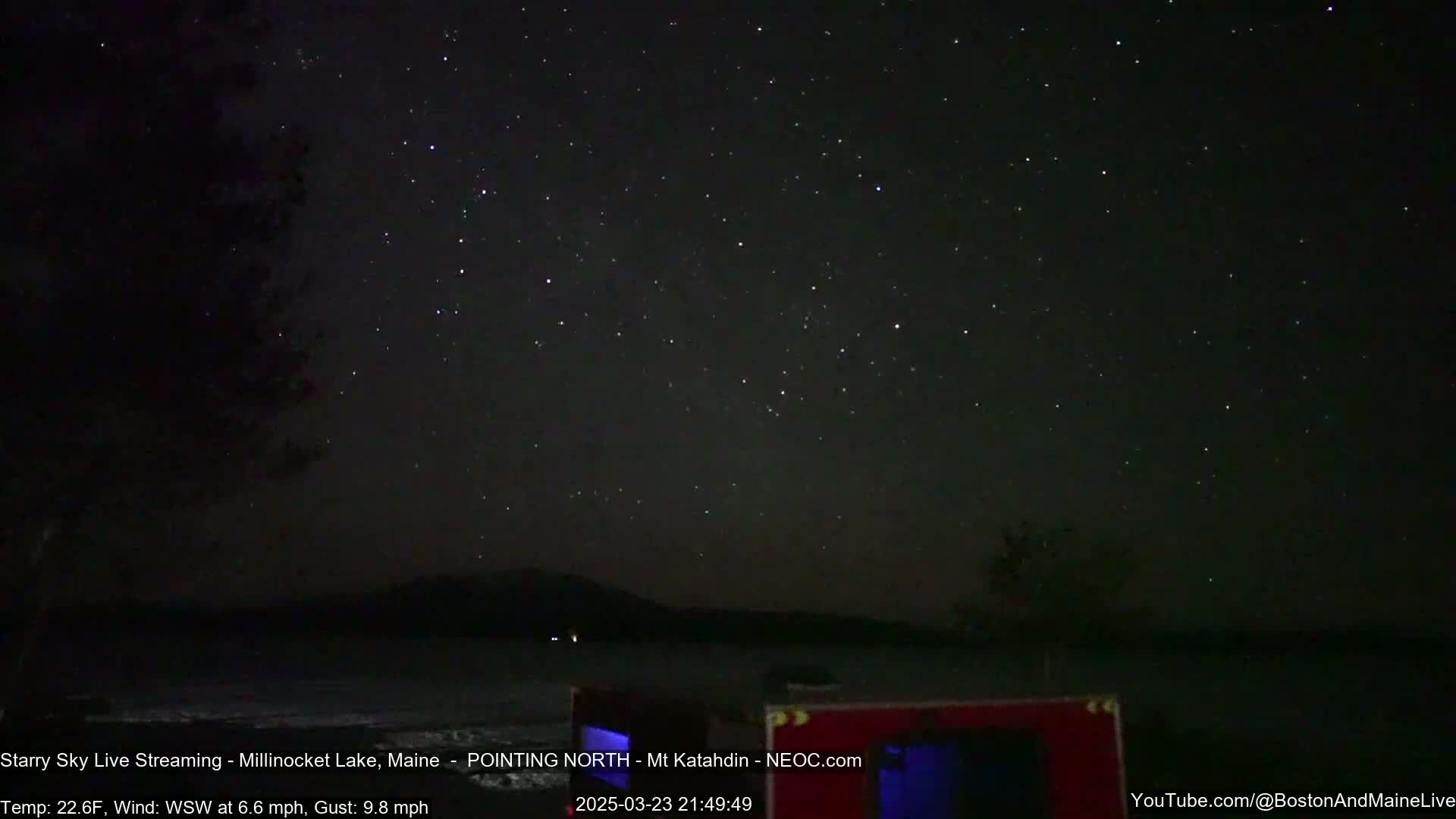A dark, starry night sky over a calm lake with a distant mountain silhouette, under a temperature of 22.6°F and a WSW wind.