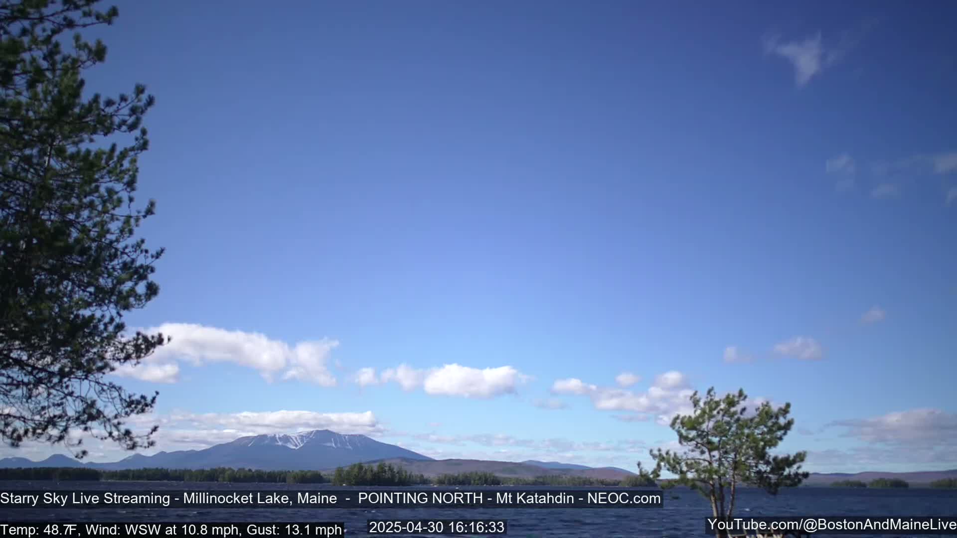 A mostly clear blue sky with a few wispy clouds over a calm lake and distant mountains, under breezy conditions.