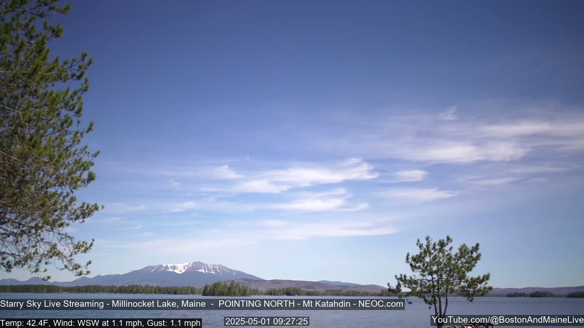 A calm lake with a snow-capped mountain in the distance under a mostly clear, light blue sky.