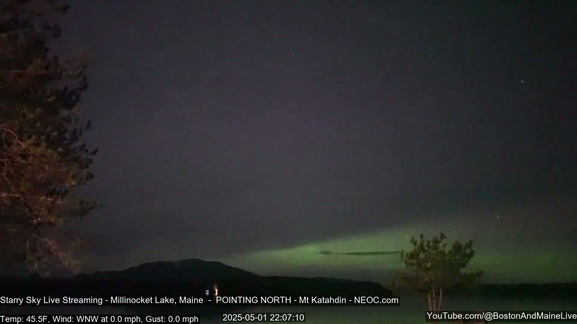 A faint green aurora borealis is visible on a dark night sky above a silhouetted landscape with trees and a mountain range.