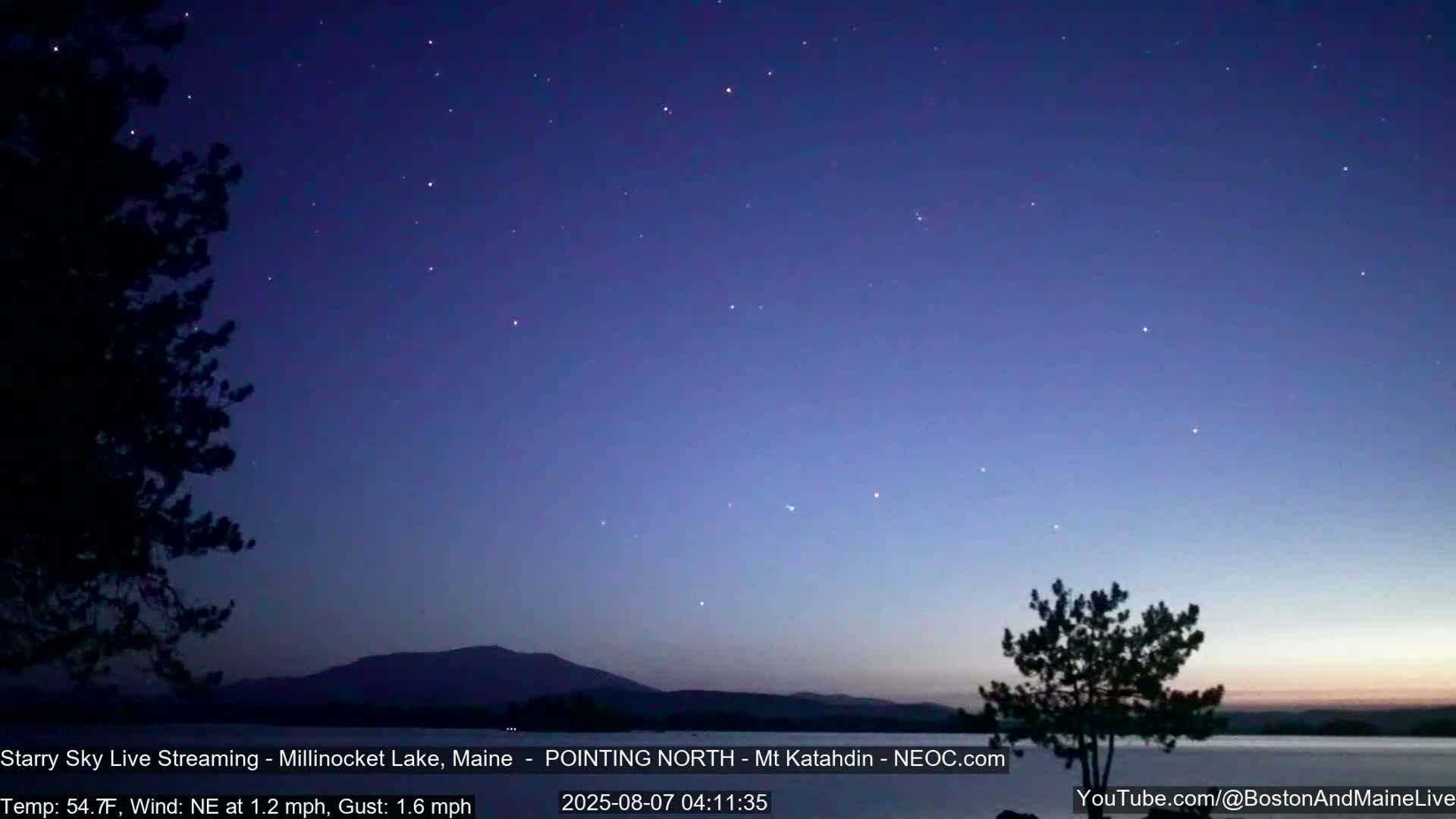 A nighttime view of a lake and mountains under a starry sky with a gentle northeast wind.
