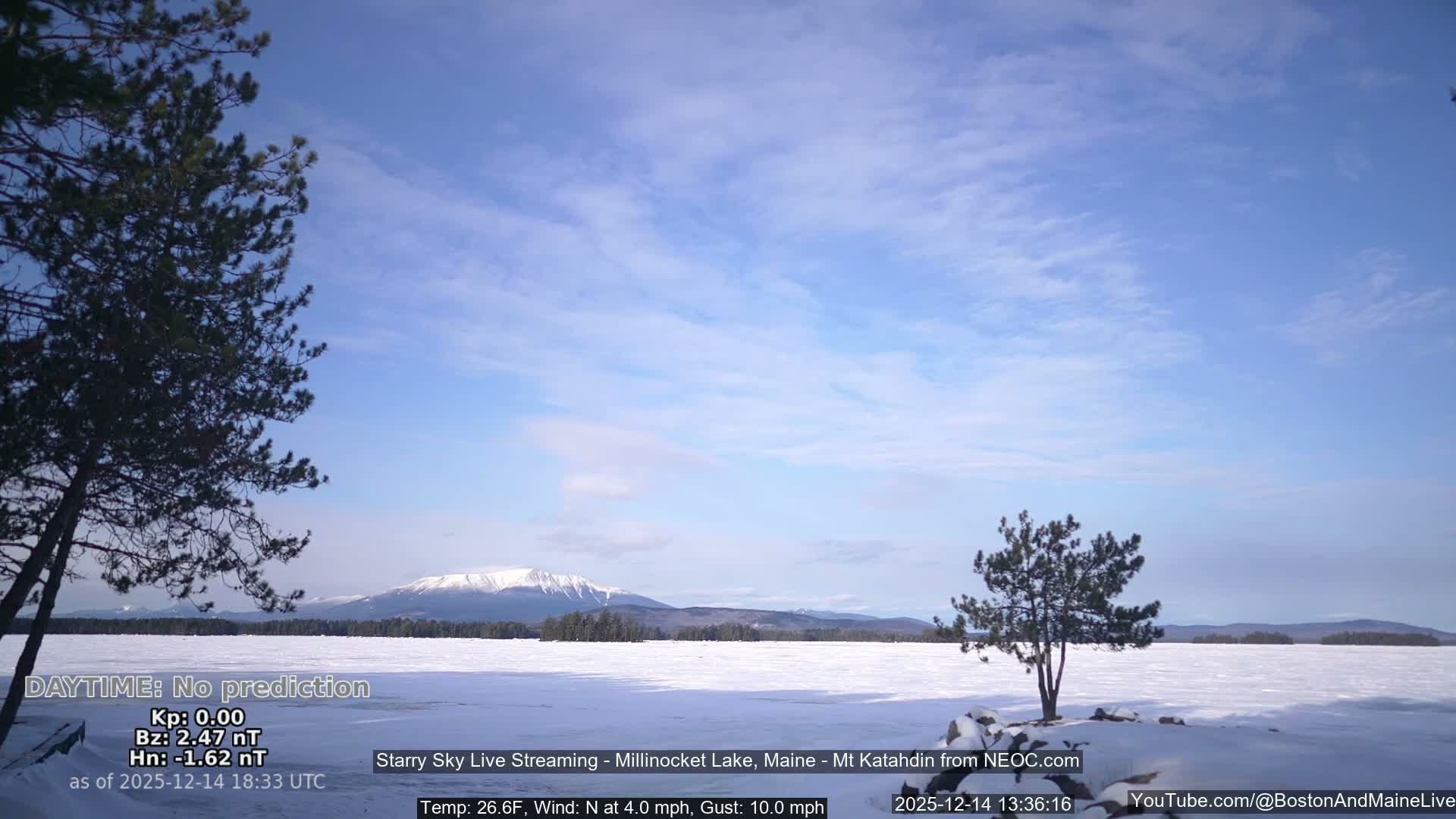 A vast, snow-covered landscape featuring a frozen lake and scattered evergreen trees is visible under a uniformly gray and hazy overcast sky, indicating a cold winter day.