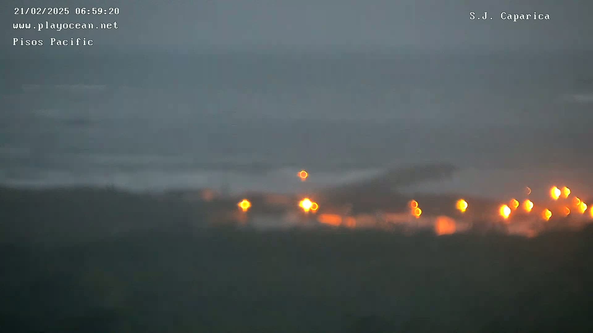 A blurry, dark image shows an overcast sky over a body of water, with a line of out-of-focus orange lights visible near the bottom.