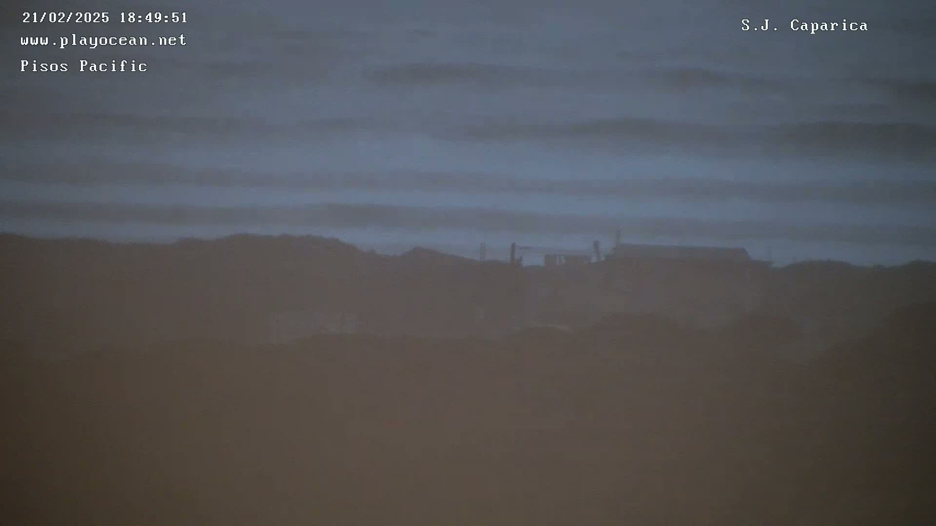 A hazy, dusky view shows distant buildings atop a hill under a muted, cloudy sky.