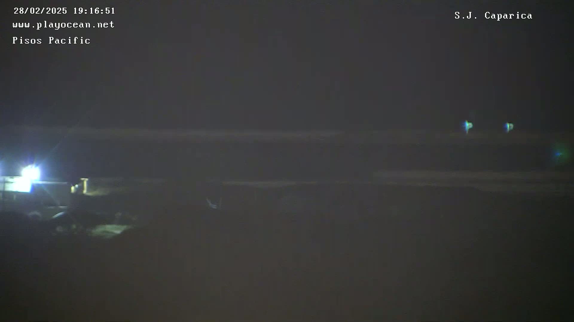 A nighttime, dark view of a beach with faintly visible waves and a bright light source in the bottom left corner.