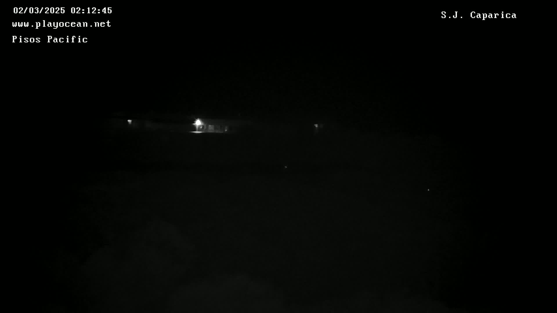 A dark, nighttime scene shows dimly lit buildings in the distance under a clear sky.