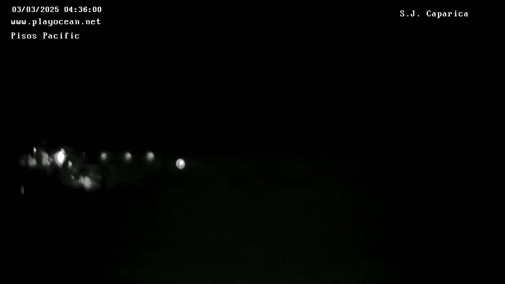 A nighttime, low-light image shows a series of blurred white lights in a horizontal line across a dark background.