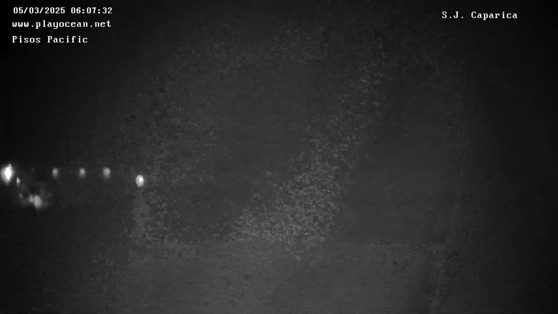 A nighttime, low-light image shows a dark, textured surface with several small, bright lights visible in the distance.